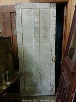 Full view of old wooden door painted white with peeling paint and wear marks.
