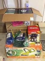 Overall view of the lot showing boxes with hedge trimmer, insect trap, garden boots and sprayers