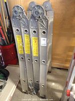 Folded ladder leaning against wall, visible four-section aluminum rails and top pulleys.