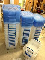 Multiple tall stacks of clear plastic bins with opaque blue lids and side latches; one bin open at front.