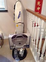 Overall view showing sealed Roomba box, charging dock and unboxed accessories in front of Oreck steamer