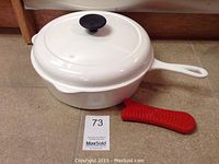White enameled skillet assembled with lid and red silicone handle cover placed alongside