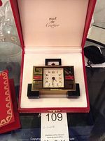 Clock inside red Cartier presentation box with white interior, lid open showing Must de Cartier logo