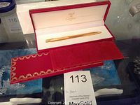 Open red Cartier case showing gold plated pen inside white lining