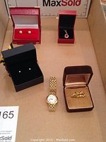 Overview shot showing two pairs of earrings, a necklace with pendant, a set of three rings, and a wristwatch