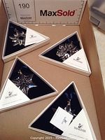 Four Swarovski triangular gift boxes each containing a different year’s snowflake ornament laid out in a cardboard tray with MaxSold ruler