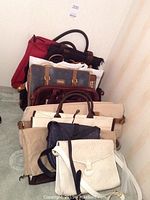 Front view of stacked handbags showing cream flap bag, navy crossbody, beige canvas tote, burgundy leather, brown suede tote, grey patterned tote, red zip-top tote and black nylon bag