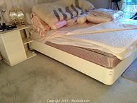 White bed frame with mattress, bedding, and sheepskin draped on top
