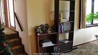 Photo showing both bookcases side by side in a living room setting near stairs and window with carpeted floor.