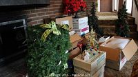Wide view showing multiple artificial Christmas trees, a large decorated wreath, poinsettia flowers, and various boxes with holiday items.