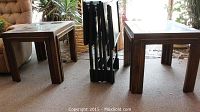 Two wooden end tables with square glass inset tops and four black foldable TV trays between them.