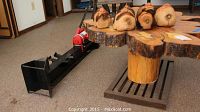 Side view of the log splitter and tree stump table with six carved coconut heads on top.