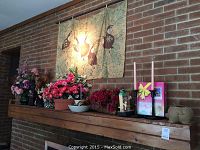 Wide view of mantle with various items including artificial flowers, banner, liquor dispenser, and bellows