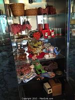 Glass shelving unit displaying decorative items including baskets, silk flowers, candles, small glassware, ceramic decor, miniature flags, fabric holiday pillows, a toy train, and other assorted items.
