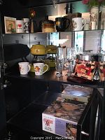 Wide shot showing cabinet contents including punch set on right side, mugs, fondue pot, and yellow stand mixer on middle shelves.