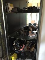 Glass cabinet listing Nikon and Vivitar cameras, lenses and accessories arranged on three shelves.