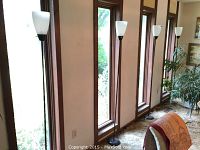 Five identical floor lamps lined along windows, showing height and style with white plastic shades and dark slim metal stands.