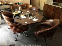 Photo of wood kitchen table with four leather and metal rolling chairs around it, showing the full set and colors of items.