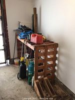 Photo showing wooden workbench with various garden and fuel containers on and below it.