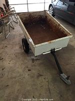 Full view of rusted small trailer with black hitch attached, showing interior and wheels.