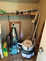 Closet corner with Kenmore Heavy Duty carpet cleaner, vacuum cleaner, and plumbing pipes on shelf above