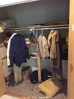 Wide angle photo of closet showing a variety of hanging coats and clothes, folded textiles on upper shelf, and some items on floor.