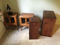 Four wooden furniture pieces on floor against wall including two night stands with glass doors, small dresser, and smaller night stand with drawers.