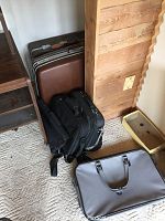Photo showing various suitcases and bags arranged near a wooden wall and shelving unit.