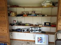 Wide view of wall shelving holding various boxed games, boom boxes, tennis balls, and other items