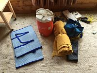 Wide view of lot showing folded tarp, drink cooler, rolled yellow pads, rope, and bags on carpeted floor.