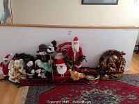 Wide view of assorted fall and Christmas figurines including Santas, angels, snowmen, wreath, and holiday signs grouped on the floor.