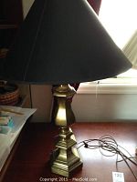 Brass table lamp with black shade on wooden surface near window