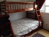 Wooden bunk bed with ladder on the right side, upper and lower mattresses visible, white bedding. Storage shelves visible beneath lower bunk.