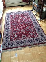 Full top view of a red Oriental rug with floral pattern, fringes visible at one end, lying on a wood floor.