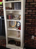 White shelving unit with several shelves displaying various collectible items including decorative plates, bowls, figurines, and coasters.