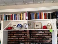 Shelf above fireplace with assorted books, Lekven plates, bowls, vases, teapots, and framed art.