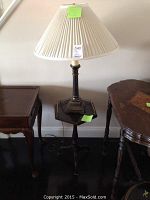 Full view of the metal lamp with pleated cream fabric shade and the small wooden table on which it is placed.