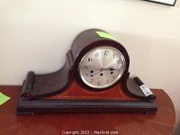 Westminster chime mantle clock with wooden curved case showing front and part of side detailing, metallic dial with three winding holes.