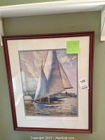 Framed watercolor style print of a sailboat with white sails on water, with dock and figure in background.