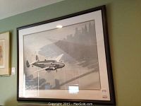 Framed black and white photograph of airplane flying over Manhattan with city skyline and water below.