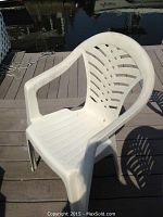 Single white plastic outdoor chair with curved armrests and vented slatted backrest, placed on a dock deck.