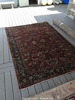 Full view of the reddish floral Oriental rug laid on a deck, showing detailed floral and border patterns.