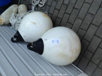Two large white spherical boat buoys with black tops laid on the ground beside a coiled white rope and additional bumper buoys, showing the overall lot contents