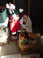 Photo showing large snowman figure, smaller Santa figure wrapped in white cloth, and bag containing vintage toy trucks and toys