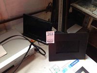 Photo showing two digital photo frames, one Polaroid IDF-0720 and one Mustek, both with remotes, displayed on a surface with related accessories.