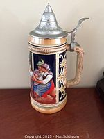 Front view showing the couple in traditional clothing embracing, pewter lid with embossed decoration, and woodgrain style handle