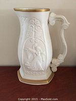 Front view of the white ceramic pitcher with raised relief scene of Romeo and Juliet and gold trim on rim and base.
