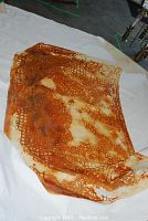 Large unstretched and unframed canvas sheet laid on white cloth showing rust-colored perforated design