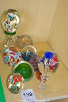 Overview photo of assorted glass paperweights and glass egg decorations on a wooden surface showing variety of shapes and colorful internal designs.