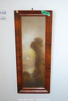 Full view of the vertically oriented signed landscape painting in a dark brown wide wood frame.